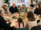 Menschen verschiedener Generationen und Lebenssituationen sitzen gemeinsam bei Kaffee und Kuchen an einem Tisch und tauschen sich aus. KI-generiertes Bild.