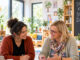 KI-generiertes Begleitbild zur Zusammenarbeit von Sozialräume e.V. mit Kitas und Familienzentren. Pädagogische Fachkräfte und eine externe Fachperson sitzen in einem hellen Familienzentrum gemeinsam an einem Tisch, tauschen sich aus und arbeiten mit Unterlagen und pädagogischen Materialien. Die Szene steht für partnerschaftliche Planung, fachlichen Austausch und die gemeinsame Entwicklung passender Angebote für Kinder, Familien und den jeweiligen Sozialraum.